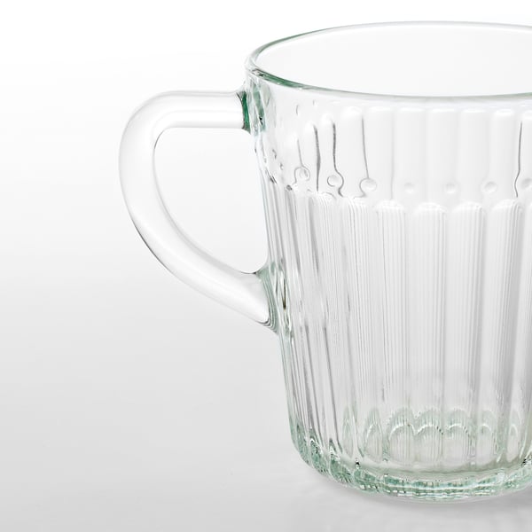 Helder glazen mok met een stevig handvat, met verticale ribbels voor grip, staande op een effen oppervlak.