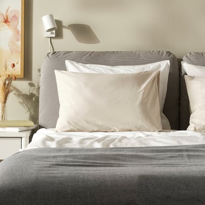 DVALA crèmekleurige kussensloop, zacht katoen, vierkante vorm, op een groot bed, met grijs hoofdeinde, eenvoudig ontwerp.