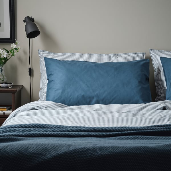 Bed met DVALA blauwe kussenslopen, gestreept dessin, groot tegen effen muur.