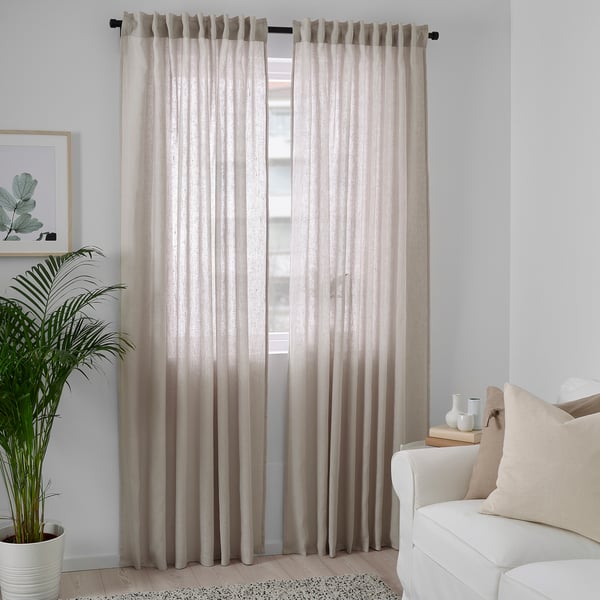 Minimalistische kamer met lichtbeige DYTÅG linnen gordijnen, witte bank en grote plant.