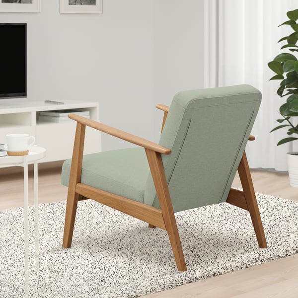 Fauteuil: EKENÄSET in groene stof en hout, op gespikkeld tapijt bij bijzettafel met mok, tv en plant.