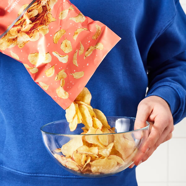Persoon die rustieke aardappelchips van rood pak in duidelijke kom giet.