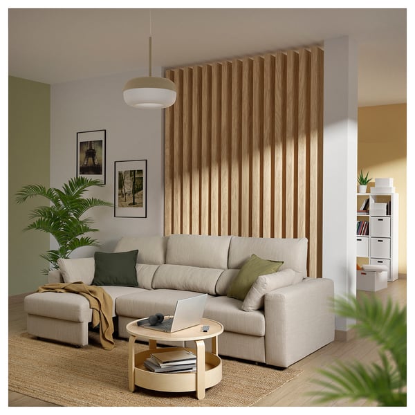 Moderne woonkamer met beige ESKILSTUNA bank, houten scheidingswand, witte salontafel, planten, gezellige kussens en scheidingswand.