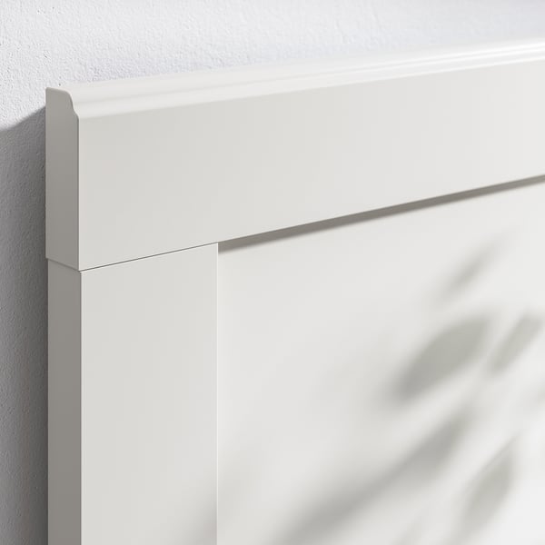 Close-up van een wit houten bedframe met strakke lijnen en een gladde afwerking.