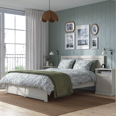 Slaapkamerset: wit bed, groene deken, houten tafel, lamp, kunst, raamgordijnen.