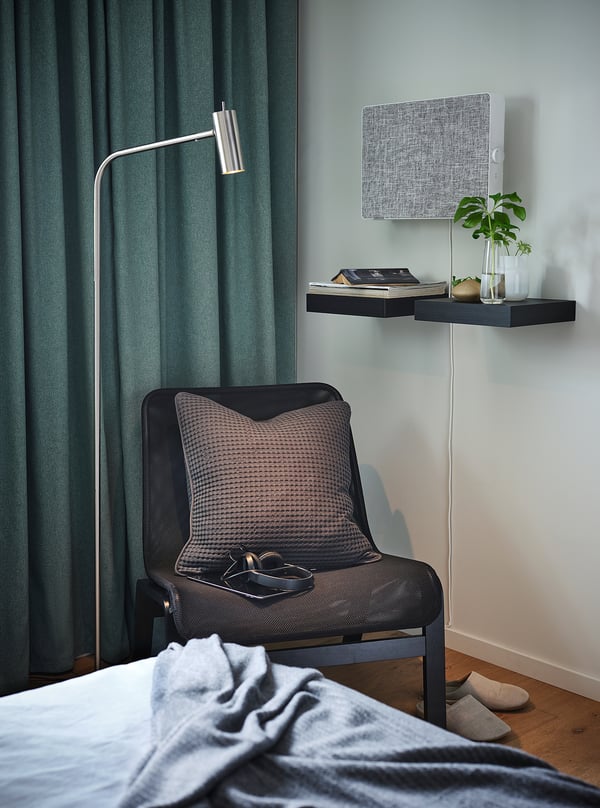 Knus hoekje met grijze fauteuil, bijzettafel en luchtreiniger. Donkergroene gordijnen, lichtblauwe muur en moderne inrichting.