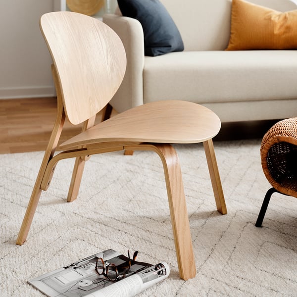 Minimalistische lichthouten stoel in de buurt van crèmekleurige bank, met beige tapijt en tijdschrift.