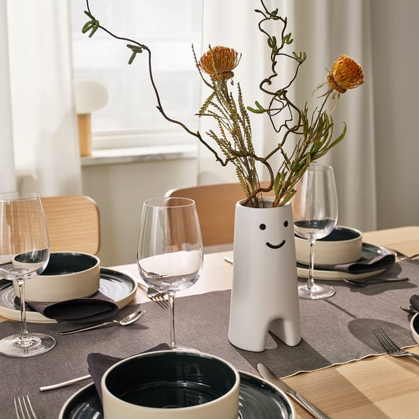 Decor: lachende bloemenvaas met oranje bloemen en glazen op tafel.