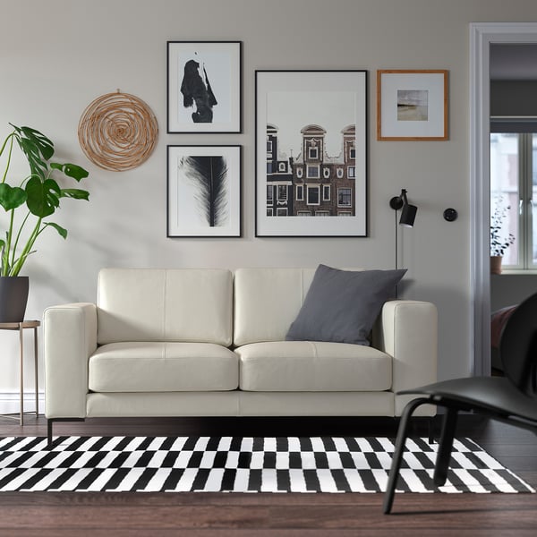 Moderne woonkamer met grijze bank, geruit tapijt, galerijwand, plant en kleine tafel.