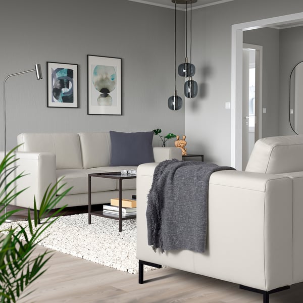 Moderne woonkamer met FULLERÖ bank, grijze plaids, blauw kussen, kunst, hanglampen, houten vloer en plant.