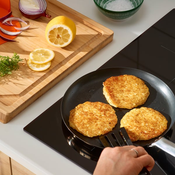 Het omdraaien van aardappelpannenkoekjes in zwarte pan. Citroen, ui, kruiden in de buurt.