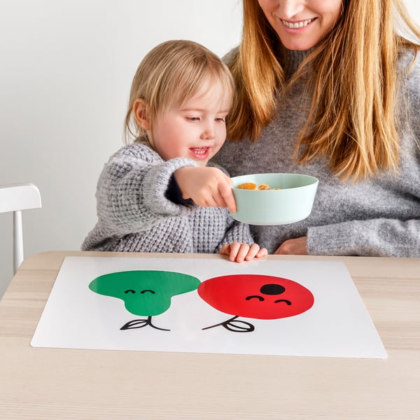 Kind in grijze trui eten van groene kom met vrouw. De tafel heeft een GRÖNFINK placemat met paddenstoelen.