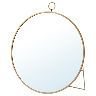 Een ronde, messingkleurige GRYTÅS spiegel met een metalen frame en standaard. Het kan hangen of staan en voegt elegantie toe aan elke ruimte.