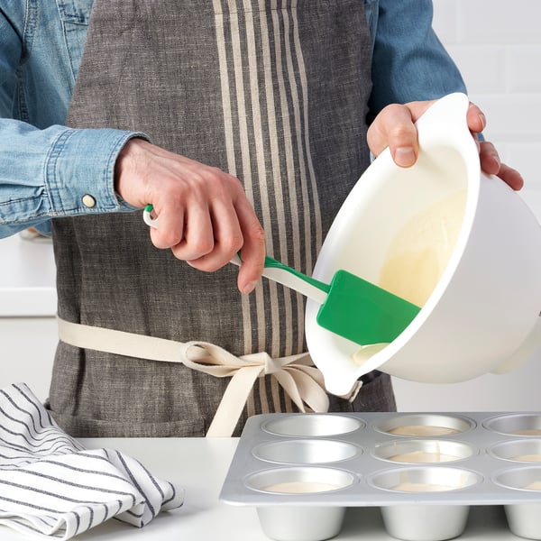 De persoon giet beslag in muffinvorm gebruikend een groene spatel.