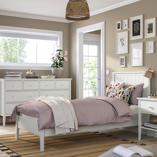 Slaapkamer met Gullberg-bed, gestreepte linnengoed, houten hoofdeinde. Gullberg-kist, nachtkastje, bloemenkussens. Raam, spiegel, kunstwerk.