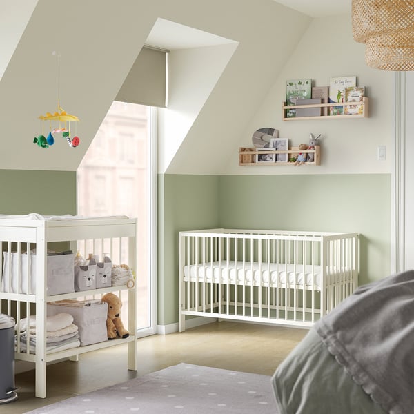 Moderne kinderkamer met witte GULLIVER wieg en wisselaar, groene accenten en kleurrijke mobielen.