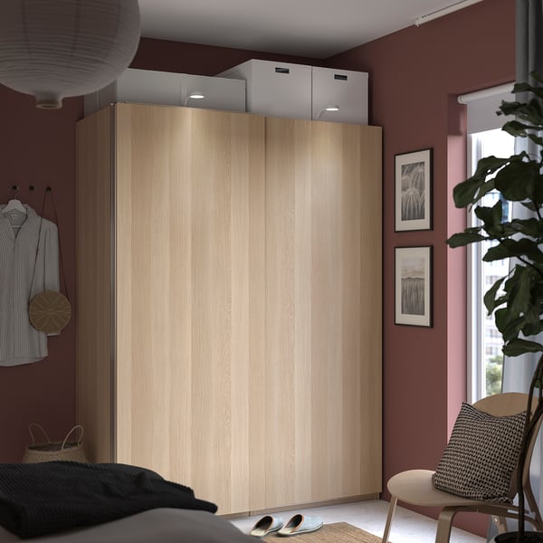Een moderne slaapkamer met een lichte houten HASVIK schuifkast, donkerrode muren en een groot raam.