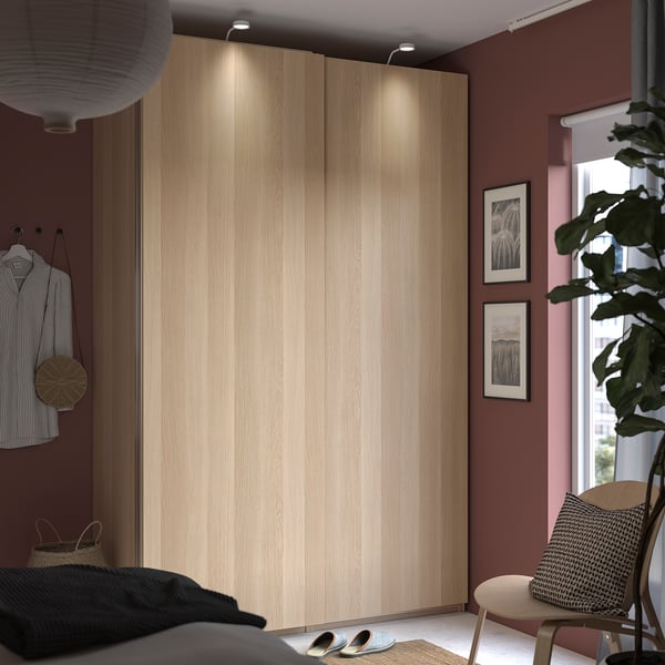 Eigentijdse slaapkamer met lichthouten HASVIK kastdeuren, gestreepte overhemdhanger, raam, schoenenrek, planten en stoel.