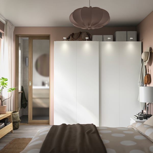 Moderne slaapkamer met grote witte HASVIK schuifkasten, een zachtbruine inrichting en beddengoed met stippen.