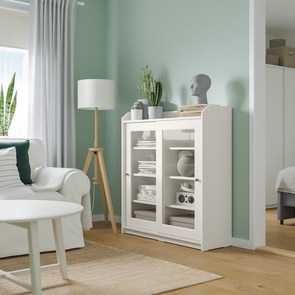 Lichte moderne woonkamer met mintkleurige muren, witte meubels en veel lichtinval. In het midden staat een witte HAUGA kast met glazen deuren.
