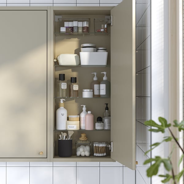 Een beige wandkast met glazen planken, waarin verschillende toiletartikelen zoals flessen, potten en borstels kunnen worden opgeborgen. Scharnierende kleppen sluiten de deur geruisloos.
