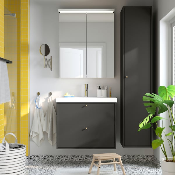 Moderne badkamer met grijze HAVBÄCK wastafel, witte wastafel, grote spiegel, potplant en een geel betegelde doucheruimte.