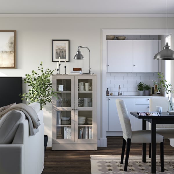 Moderne leefruimte met HAVSTA lichte houten vitrinekast, witte keuken, eettafel en grijze bank.