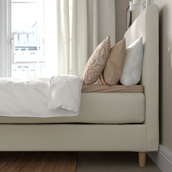 Een modern bed met zacht hoofdeinde biedt rugsteun om te lezen; Witte lakens en kussens met patronen voegen comfort en stijl toe.