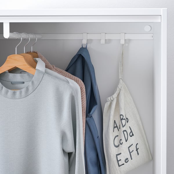 Witte kledingroede in ondiepe kast; Biedt plaats aan verschillende hangende kledingstukken, waaronder een grijze trui en een blauw jasje.