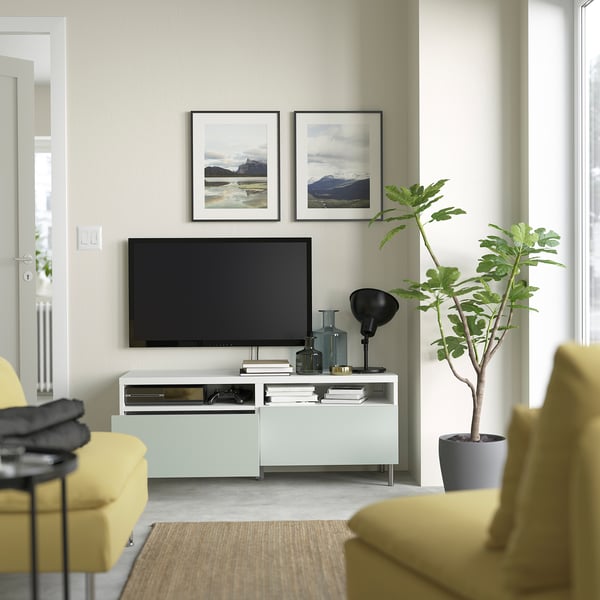 Moderne woonkamer met HJORTVIKEN tv-meubel, gele stoelen, grote plant, lamp, kunst aan de muur en zwarte tv.