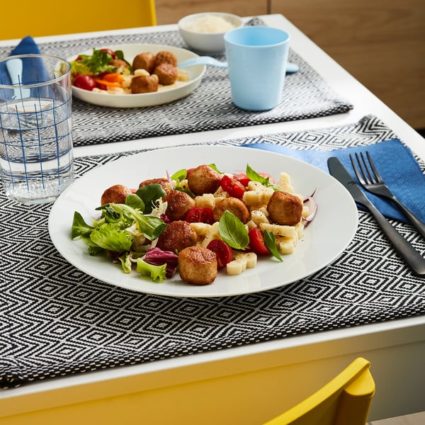 Een maaltijd met kipgehaktballetjes, salade en een drankje op een tafel met blauwe en witte couverts.