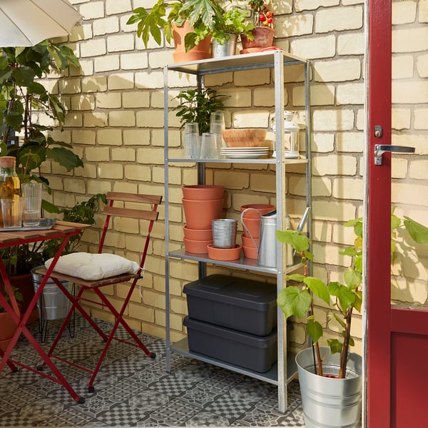 Metalen buitenplank met rode accenten en planten tegen bakstenen muur.