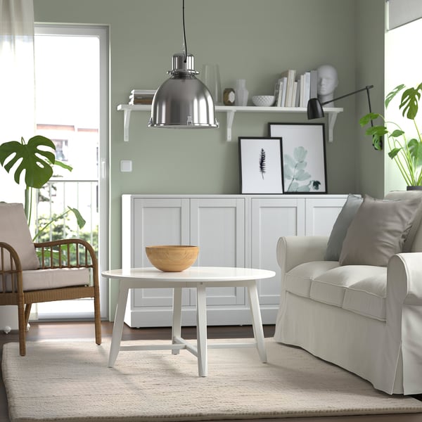 Woonkamer met groene muren, witte salontafel, stoelen, vloerkleed en versierde plank.