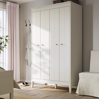 Witte IDANÄS kledingkast met tweevoudige deuren staat in een kamer. Het is strak en modern met lichte houten vloeren. Aan een haak in de buurt hangt een handdoek.