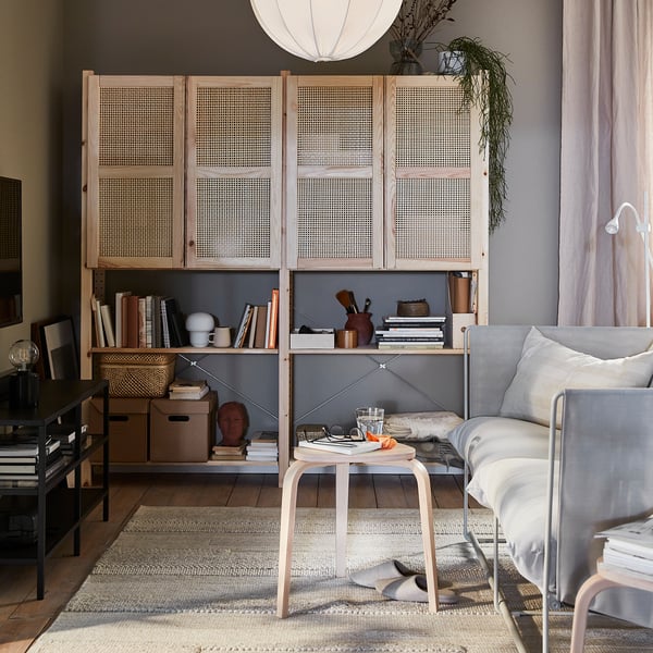 Woonkamer met IVAR rekkenkast, lichte houten deuren, boeken, inrichting en een kleine tafel, verlicht door een hanglamp.
