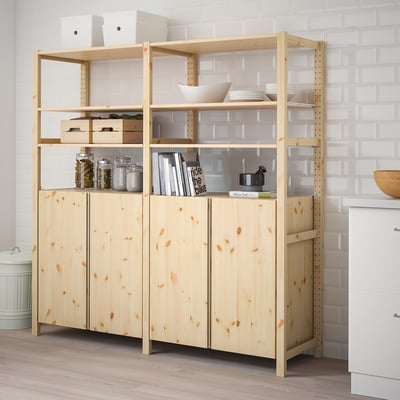 Houten IVAR opbergmeubel met planken en artikelen, naast een witte bakstenen muur.