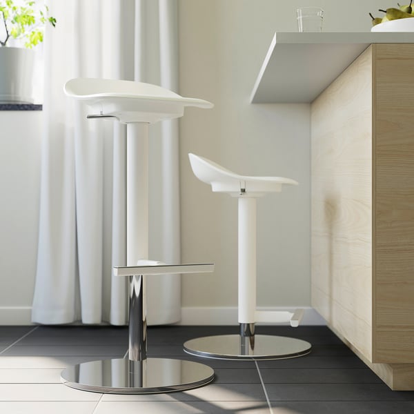 Twee moderne witte barkrukken met chromen onderstellen en voetsteunen geplaatst in een minimalistische keuken.