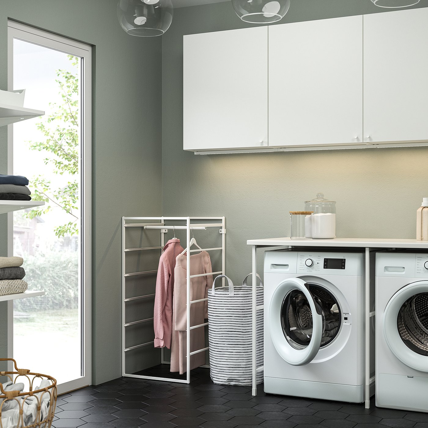 Moderne wasruimte met wit JONAXEL ophangrek met roze kledingstukken, naast witte wasmachines en kasten, met een ronde wasmand.