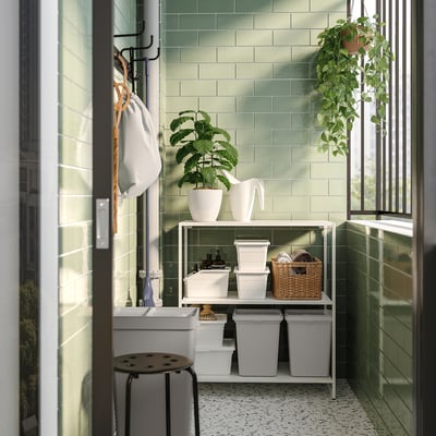 Moderne badkamer met groen betegelde muren en witte opbergplanken met containers en planten, wat de netheid en organisatie verbetert.