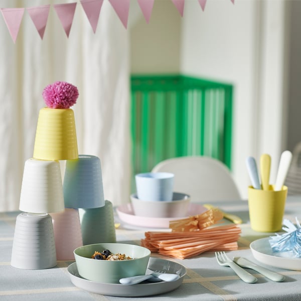 Kleurrijke plastic serviesset, inclusief gestapelde kopjes, kommen met eten en keukengerei, ontworpen voor kinderen die zelfstandig leren eten.