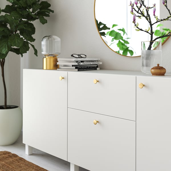Witte kast met gouden knoppen, met boeken en decoratieve artikelen. Een grote fabriek is in de buurt.