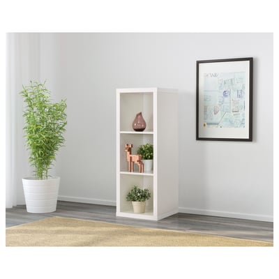 Grijs ommuurde kamer met KALLAX witte rekkenkast, met vazen en plant. Lange groene plant ernaast. Ingelijste kunst aan de muur in de buurt.