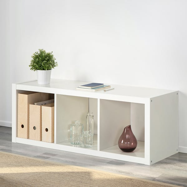 Witte KALLAX kast met opbergdozen en decoraties. Geeft veelzijdigheid en organisatorische mogelijkheden weer.