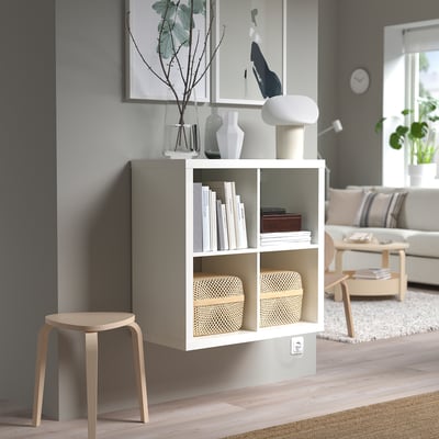 Witte KALLAX plank met boeken, vazen, lamp, naast kruk, onder fotolijst op grijze muur.