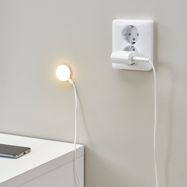 Een aan de muur gemonteerde lamp die op een stopcontact is aangesloten, straalt warm licht uit, ideaal om te lezen of een gezellig tintje toe te voegen.