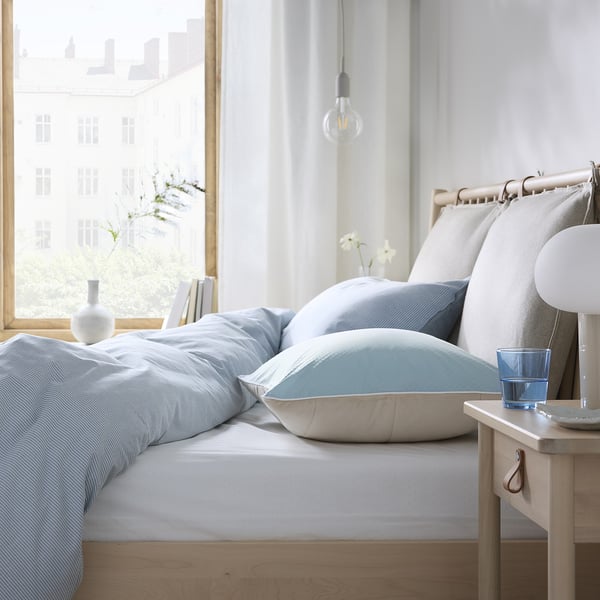 Minimalistische slaapkamer: blauw bed met witte kussens, houten nachtkastje, hangende lamp, uitzicht op de stad.