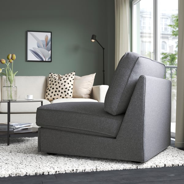 Moderne woonkamer met grijze slaapbank, wit vloerkleed, salontafel met boeken, bloemen en stippenkussen. Groot raam toont uitzicht op de stad.
