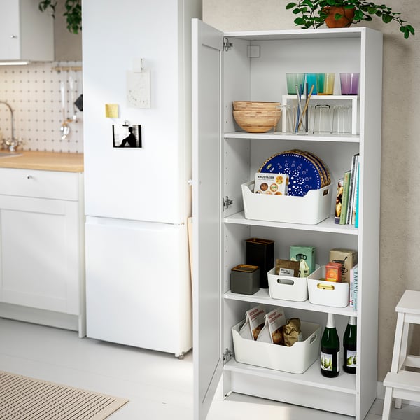 Een hoge witte keukenkast met open deuren toont netjes georganiseerde items. Het bevat kommen, glazen, dienbladen en dozen op verstelbare planken.