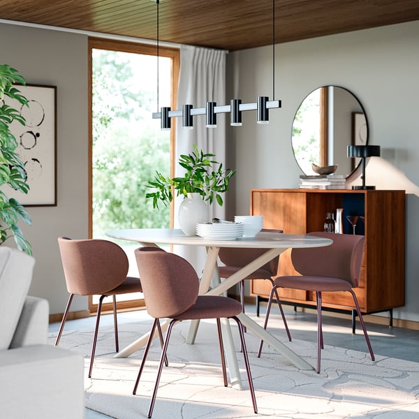 Moderne eetkamer met KRYLBO-stoelen in mauve, een ronde tafel onder een grote spiegel, omringd door houten kasten en weelderige planten.