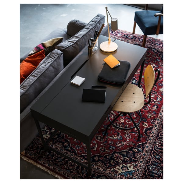 Modern thuiskantoor: verstelbare stoel, bureau, kleurrijk vloerkleed, briefpapier, lamp, laptop; Bank met kussens.